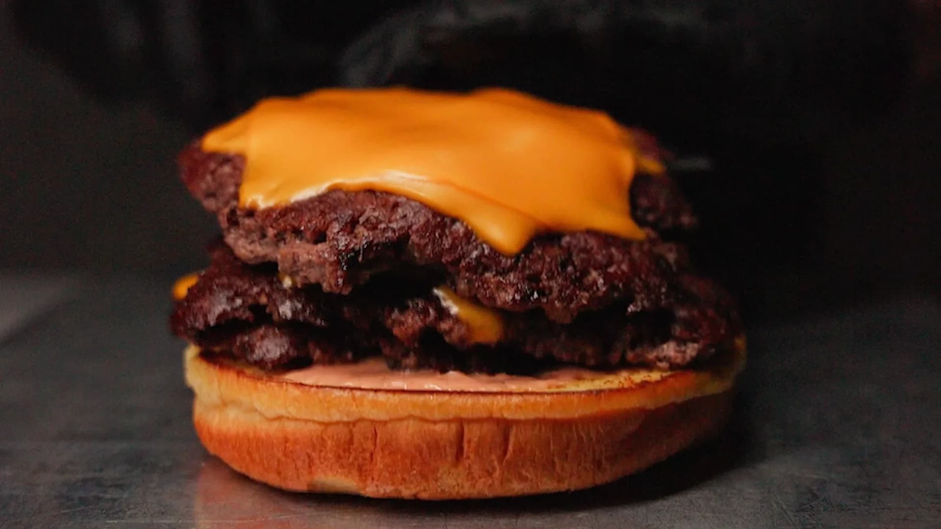 Double Smashburger mit Cheddar, frisch aufgebaut, vor dunklem Hintergrund
