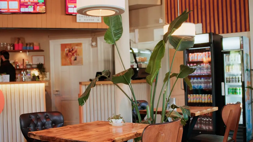 Das Lokal von innen: Holztische, warmes Licht, Pflanzen und die Theke