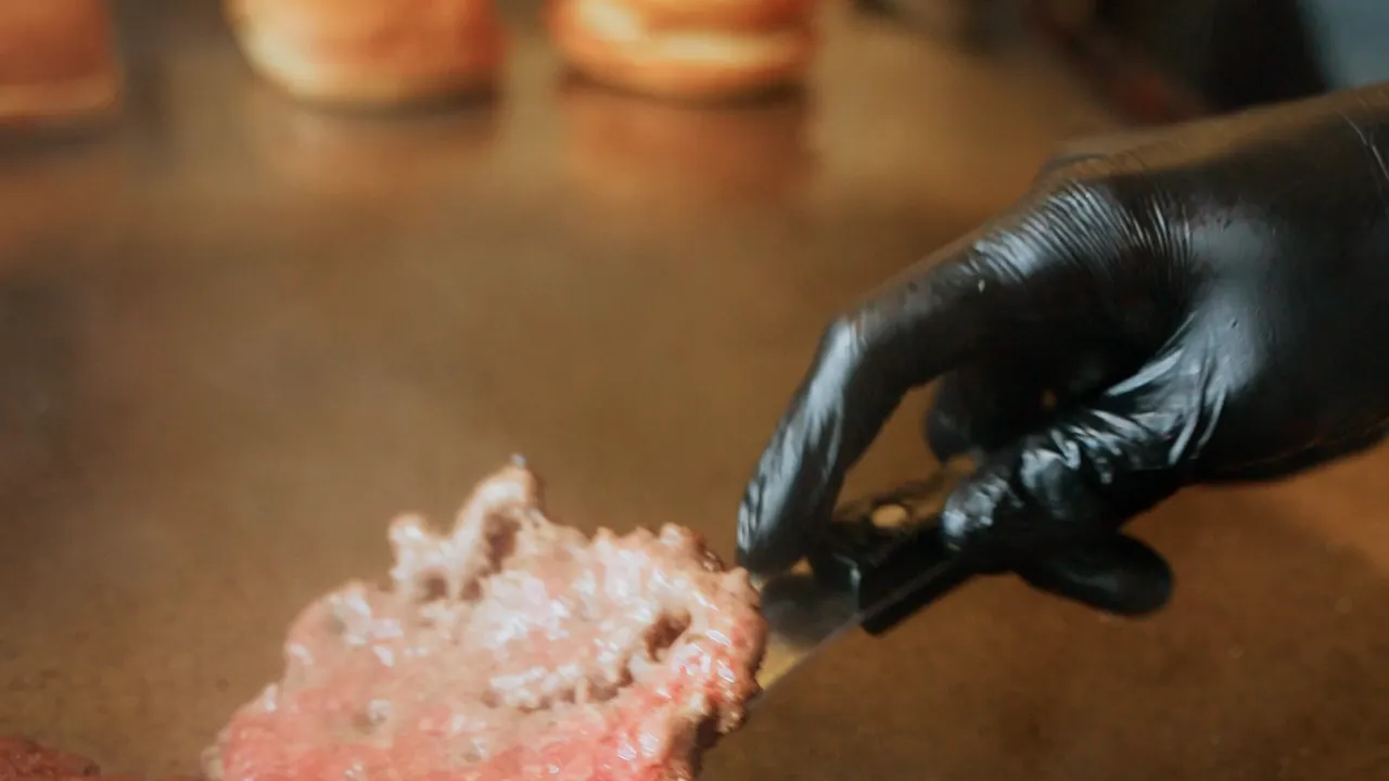 The patty being smashed and flipped on the blazing plate, then a slice of cheddar goes on